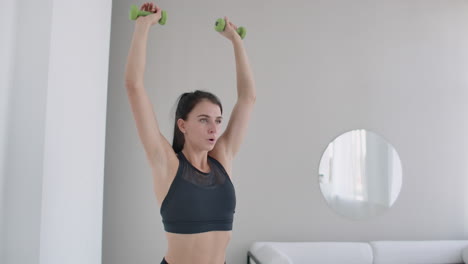Raise-the-dumbbells-over-your-head-performing-exercises-for-the-shoulders.-Training-at-home-in-the-apartment.-A-brunette-woman-with-long-hair-and-a-beautiful-figure
